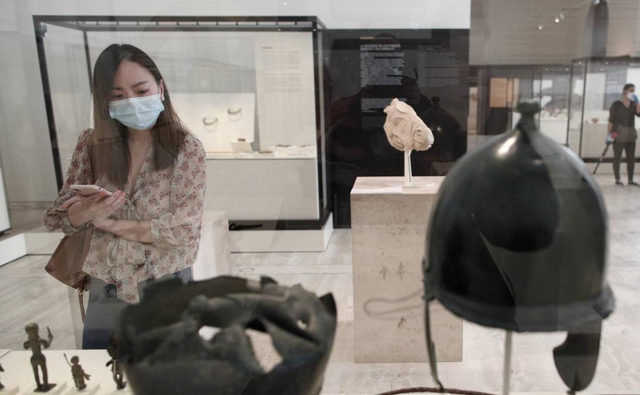 Una persona protegida con mascarilla observa las obras disponibles en el Museo Arqueológico