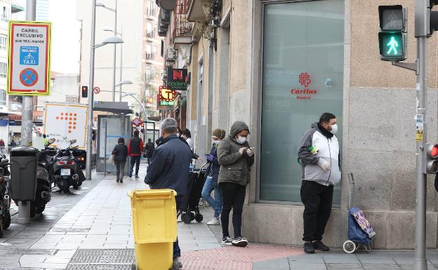 Un grupo de personas hace cola para entrar en un economato solidario de Cáritas. 