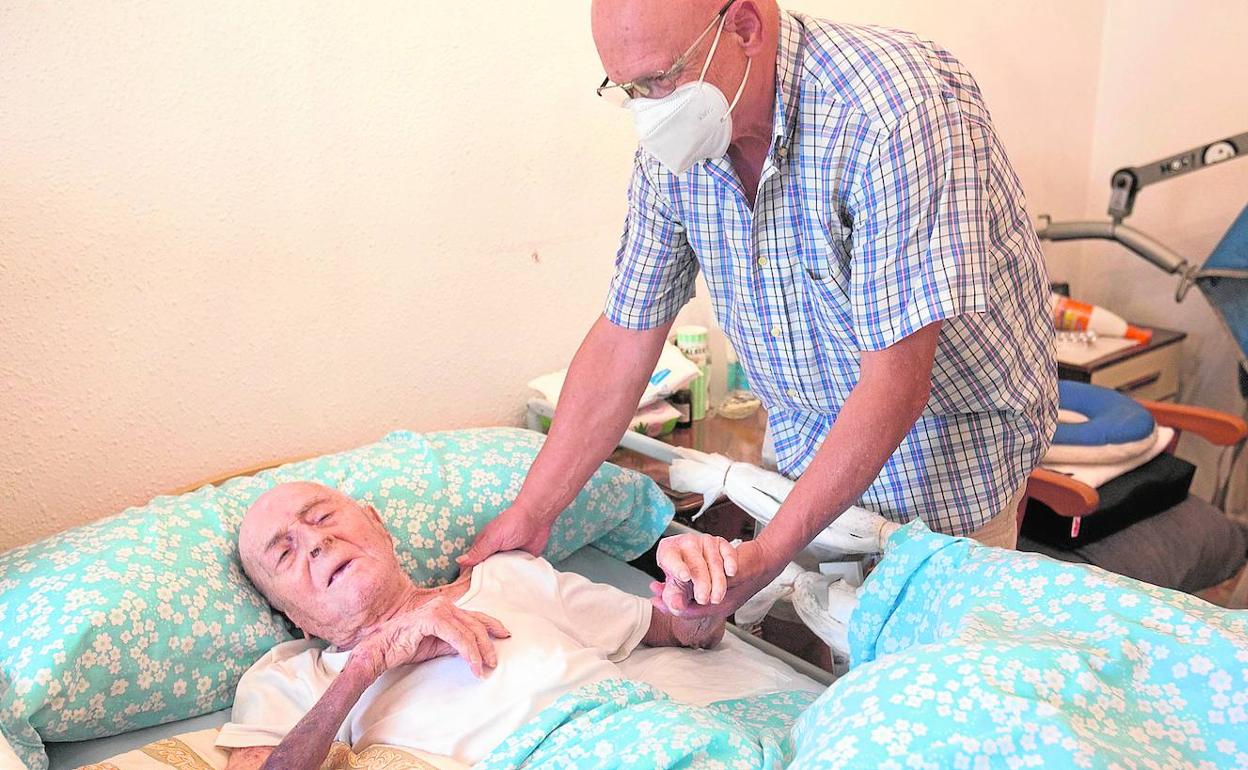 José Andreu Calvo, tendido en la cama y atendido por su hijo Juan, ayer.