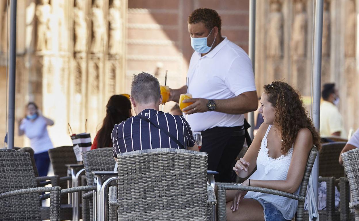 Un camarero con mascarilla atiende a dos clientes en una terraza de Valencia.