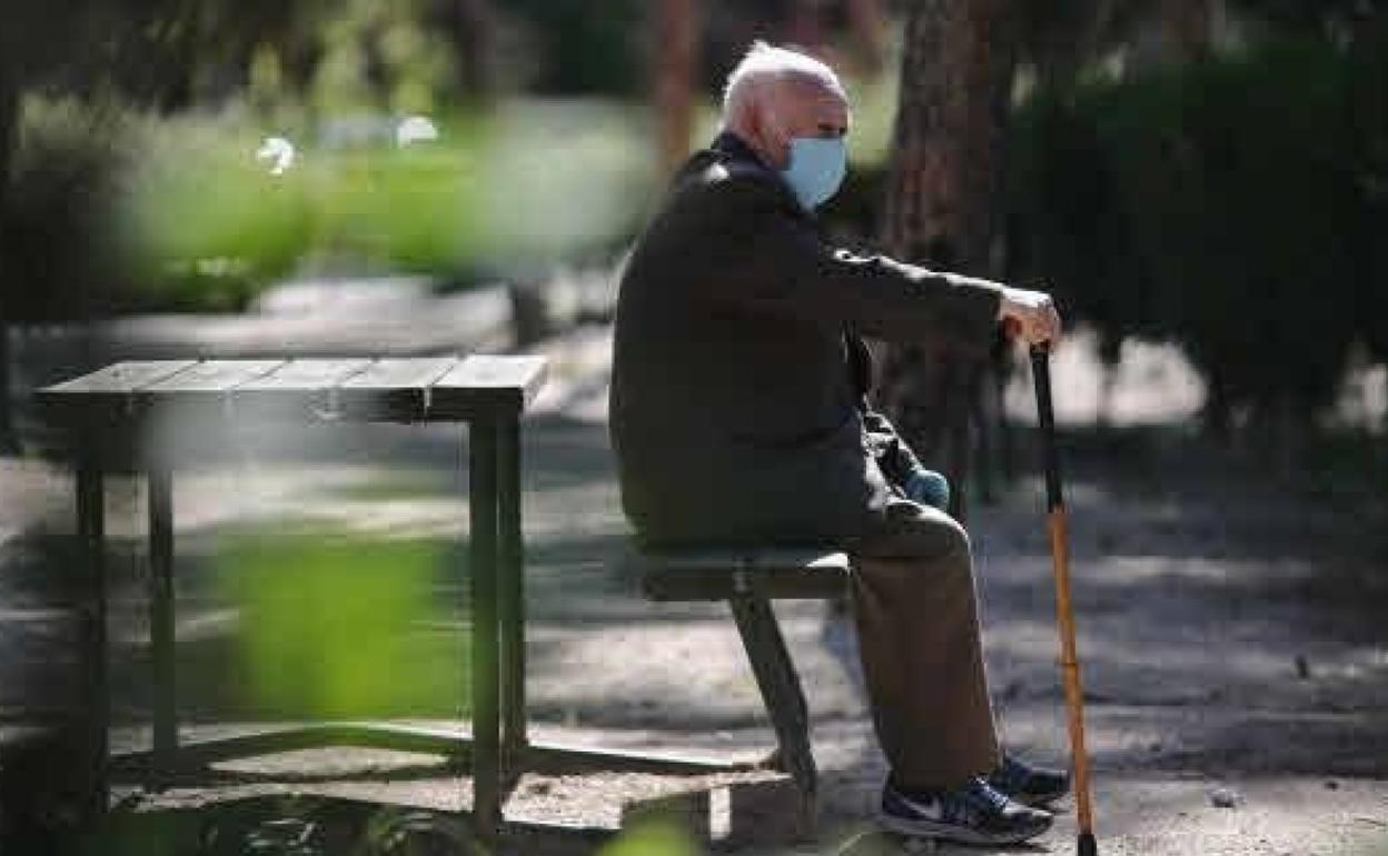 Una persona mayor, con mascarilla de protección, en un parque. 