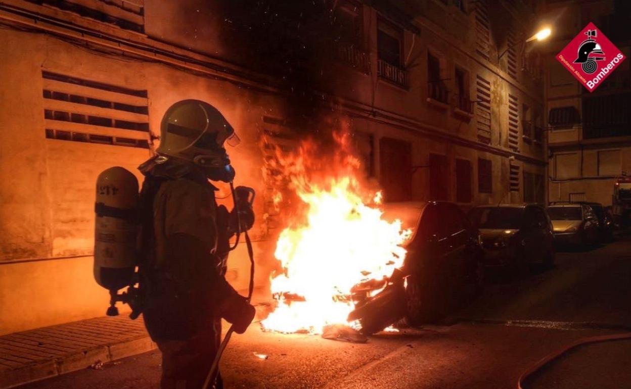 Un bombero trata de sofocar las llamas de uno de los vehículos incendiados esta noche en Elda. 