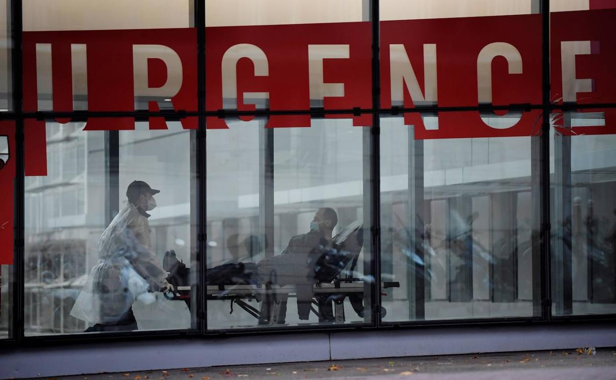 Un celador con un equipo de protección individual (EPI) traslada a un paciente en camilla hacia el servicio de Urgencias del hospital Tenon de París