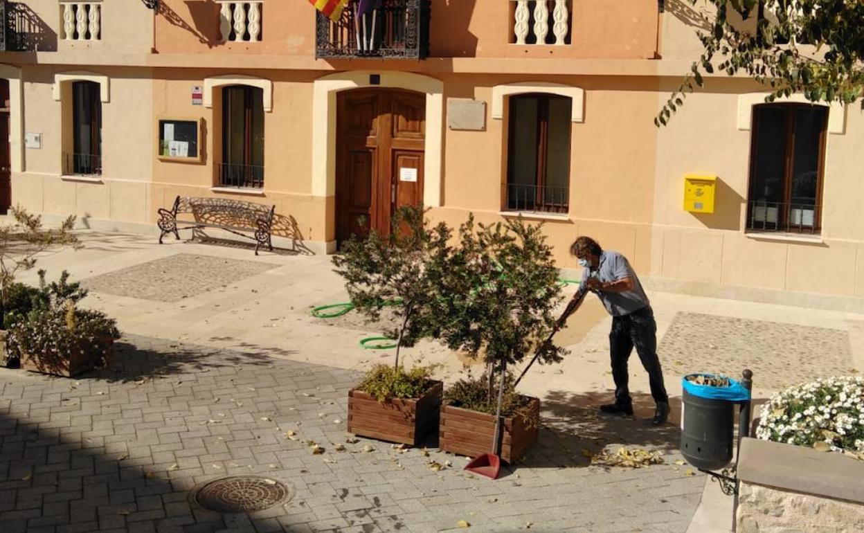 El alcalde de la Vall d'Alcalà, Pablo Martínez, barre las hojas del suelo en la plaza del Ayuntamiento.