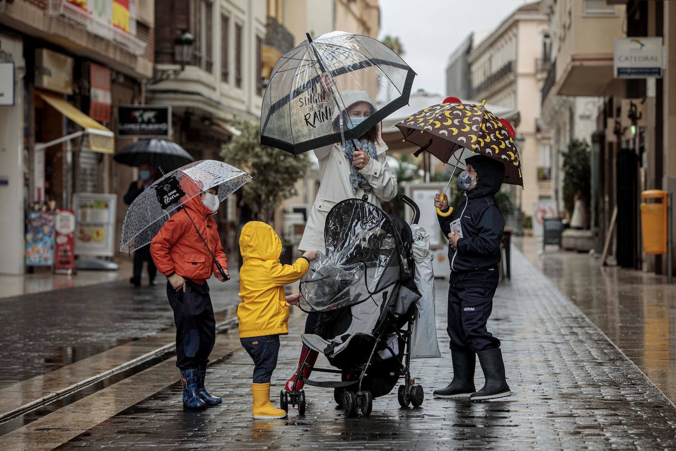 Una mujer con tres menores se protegen de la lluvia con paraguas y chubasqueros en una céntrica calle de Valencia, este miércoles.