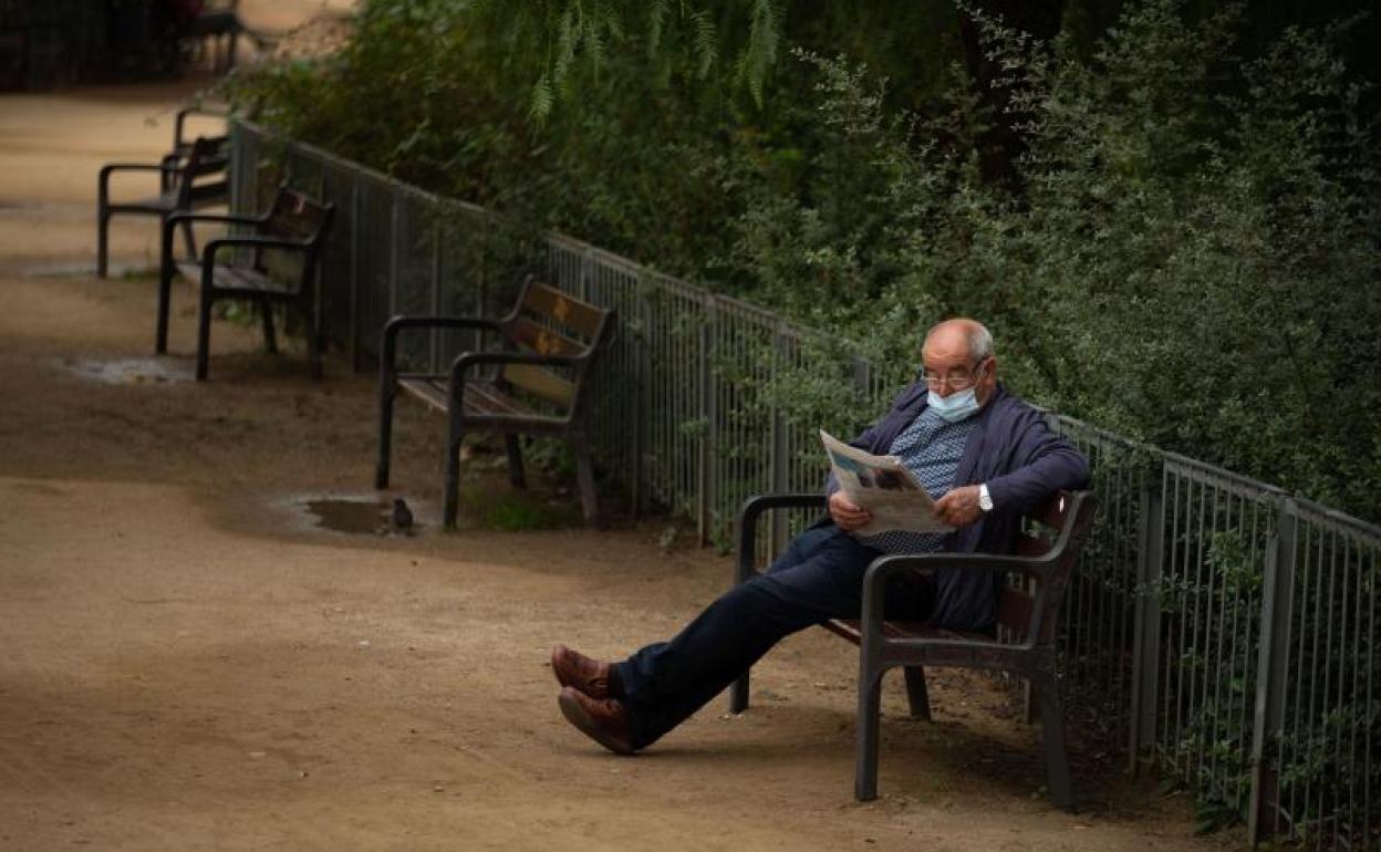 Un hombre lee el periódico en un parqu vacío.