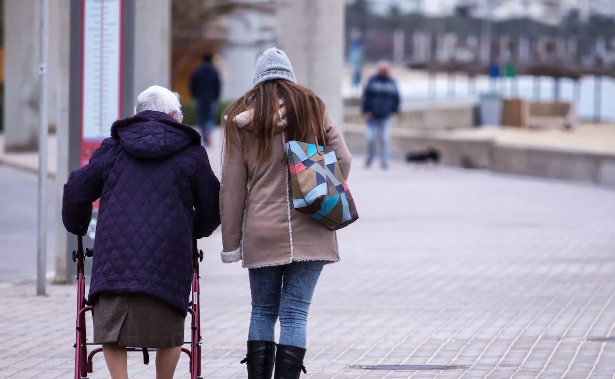 Una mujer mayor paseando con andador por un paseo marítimo. 