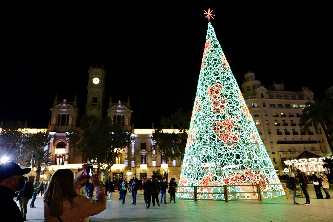 El alcalde Ribó ha asistido esta tarde al encendido en la plaza del Ayuntamiento, acompañado por las falleras mayores de Valencia, Consuelo Llobell y Carla García. La iluminación se estrena en la ciudad con quejas por el escaso gasto frente al aumento en otras ciudades para ayudar al comercio.