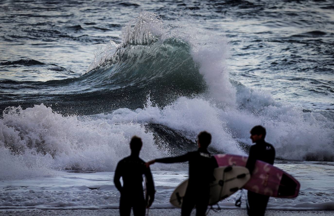 Tres surfistas se preparan para entrar al agua en la playa de La Concha de San Sebastián, aprovechando el temporal marítimo en el Cantábrico.