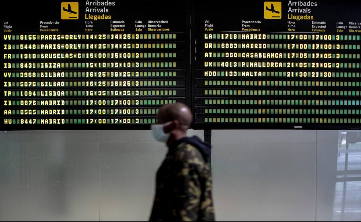 Un persona pasa frente al panel de llegadas del aeropuerto de Valencia.