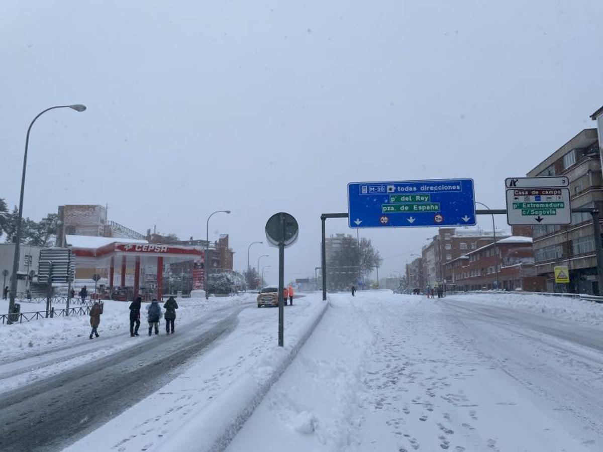 Varias personas caminan por la calzada completamente cubierta de nieve del Paseo de Extremadura a la altura de Batán en Madrid