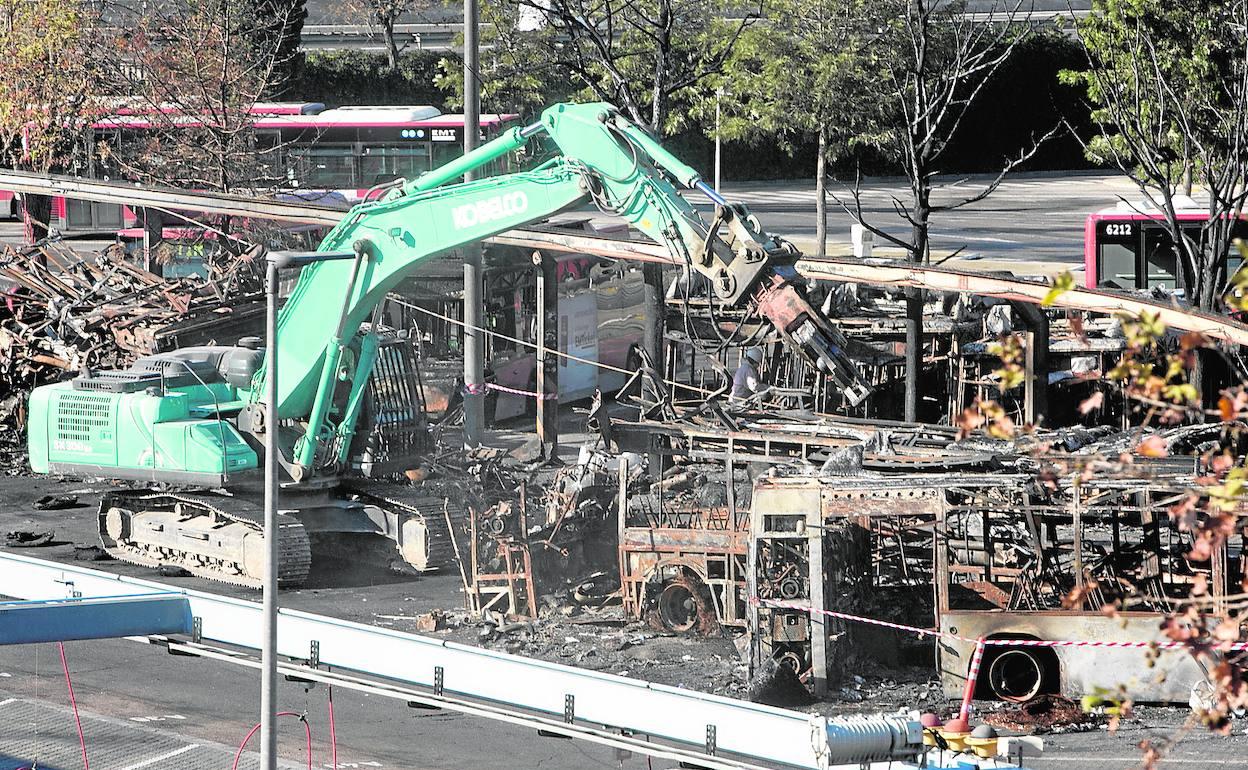 Una grúa retira un autobús incendiado de cocheras. 