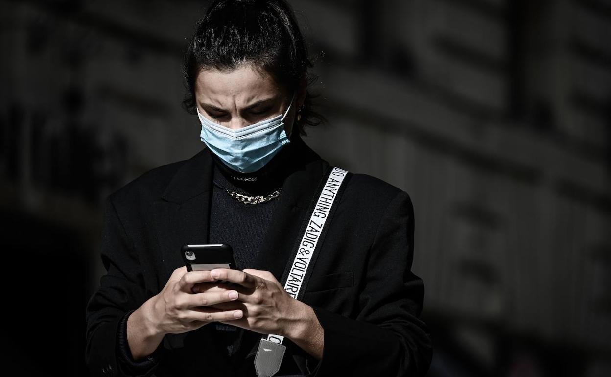 Una mujer con mascarilla camina mirando su teléfono móvil. 