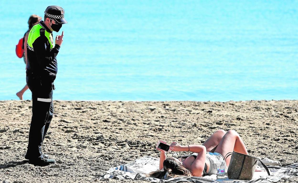 Un policía local llama la atención a una mujer por no llevar mascarilla en la playa, en Alicante. 