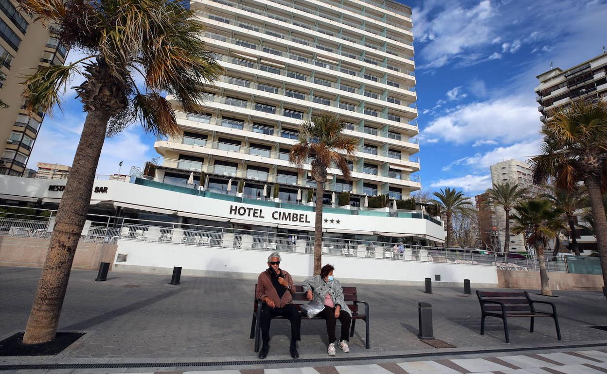 Dos personas sentadas ante un establecimiento hotelero de Benidorm. 