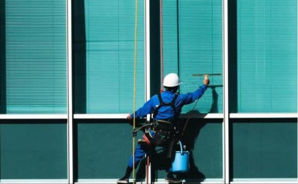 Un trabajador limpia cristales de un edificio. 