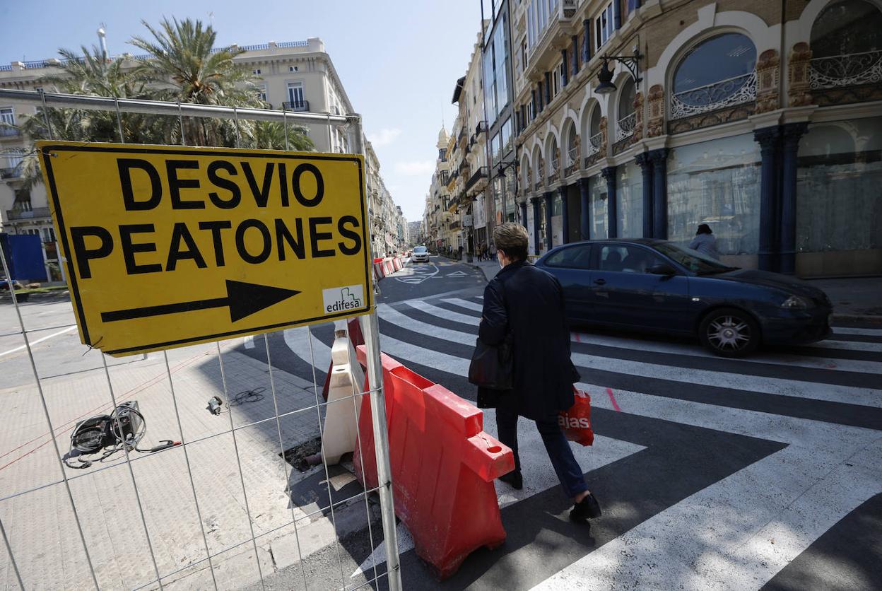 Una mujer cruza la calle junto a una valla de obras. 