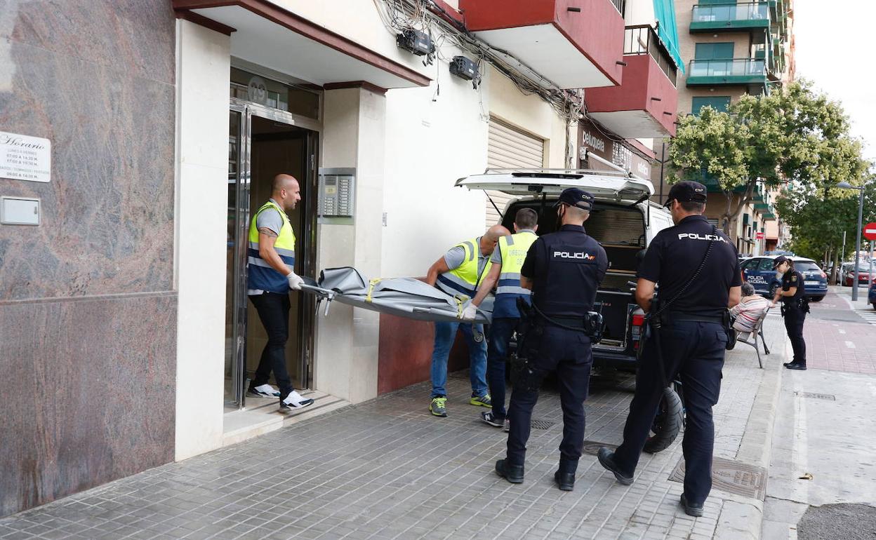 Policías ayudan a sacar el cadáver de la víctima mientras una agente consuela a la madre de los hermanos, al fondo, en un banco.