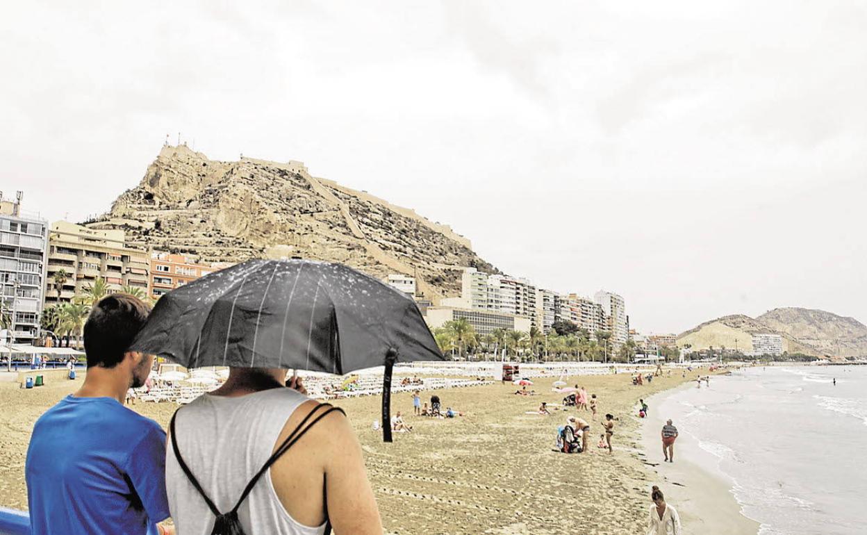 Dos turistas observan la playa del Postiguet con el castillo de Santa Bárbara al fondo. 