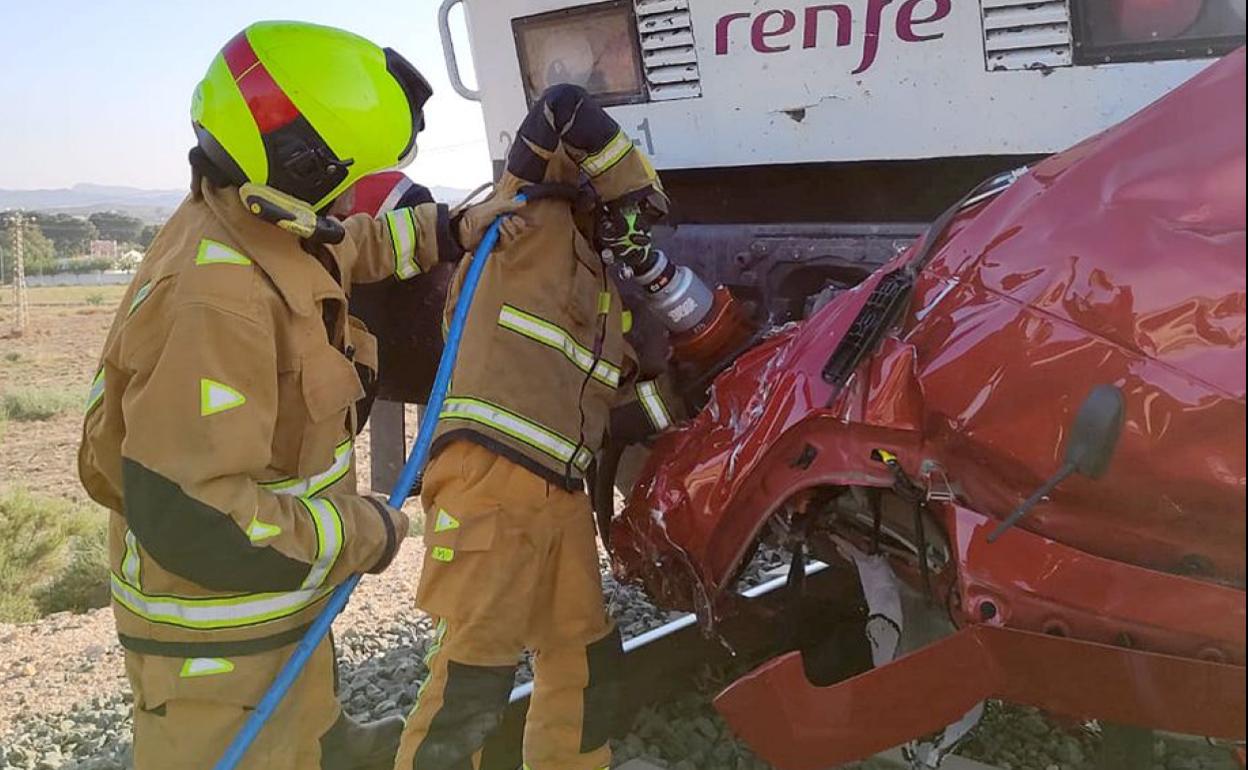Los bomberos retiran los restos del vehículo que quedaron encajados en el convoy. 