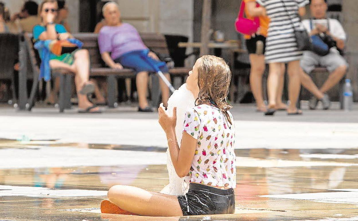 Una joven se refresca en una fuente en Alicante. 