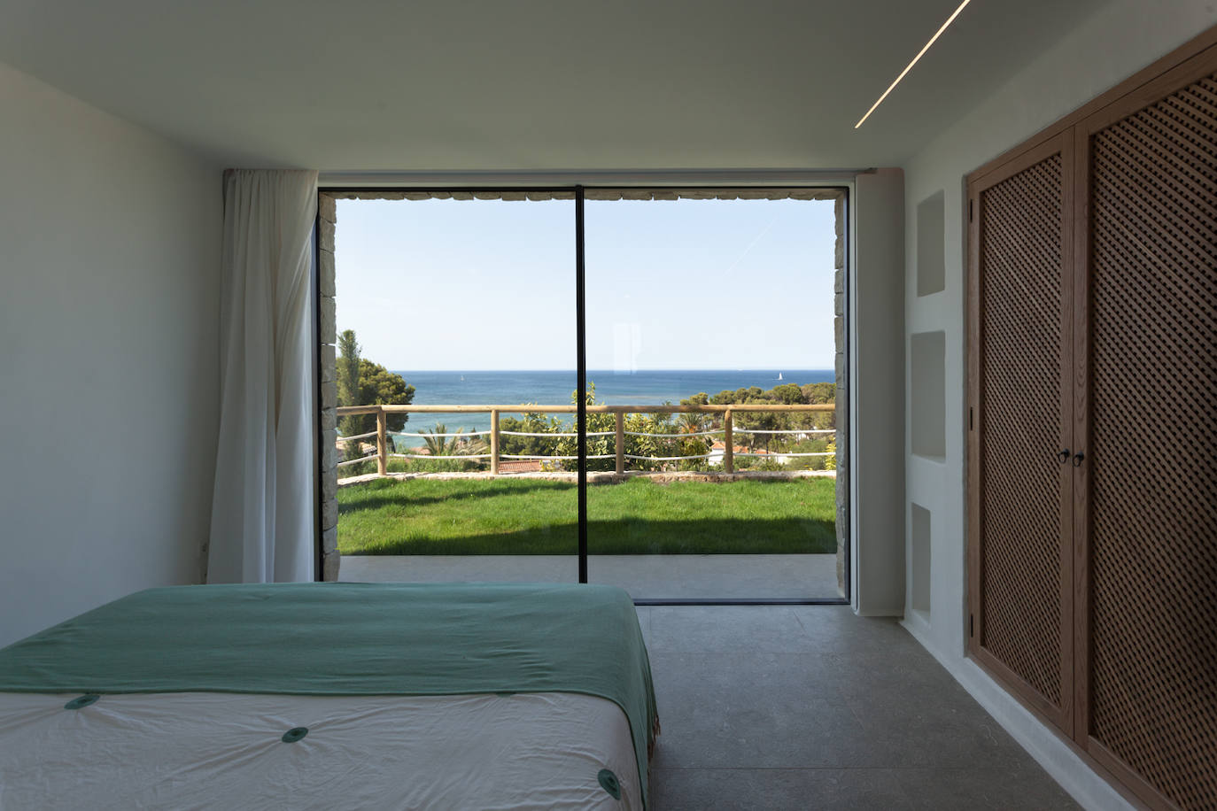 El blanco y la madera de olmo están presentes en el interior de la vivienda, en contraste con los verdes y azules del exterior.