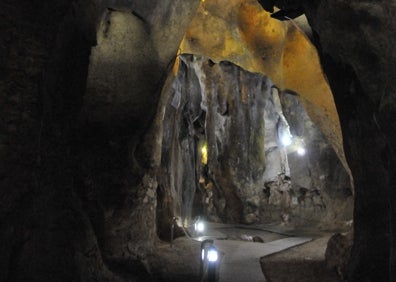 Imagen secundaria 1 - Arriba, un visitante observa los altos techos de la sala de la Ermita. Abajo a la izquierda, la plataforma de madera, que se encuentra iluminada por pequeños faroles. Abajo a la derecha, formaciones en las paredes de la gruta. 