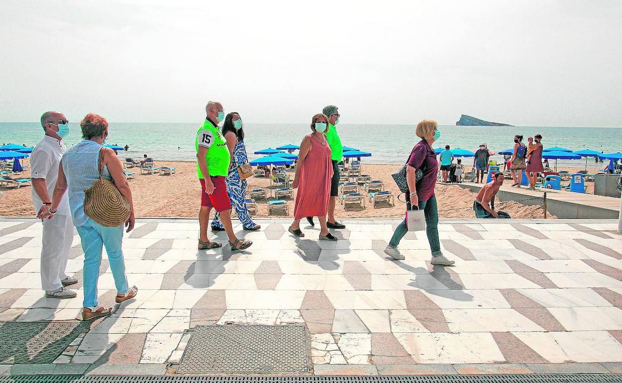 Varios turistas pasean junto a la arena en una playa de Benidorm.