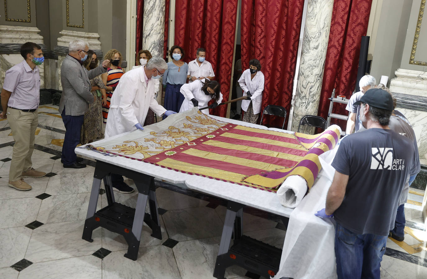 Cuatro meses de restauración devuelven el brillo a la enseña de 1928, que procesionará el 9 d'Octubre. Los expertos comprueban que el azul grisáceo que corona la pieza responde al mismo tono que muestra la bandera del siglo XVI