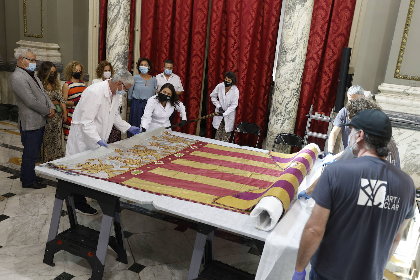 Cuatro meses de restauración devuelven el brillo a la enseña de 1928, que procesionará el 9 d'Octubre. Los expertos comprueban que el azul grisáceo que corona la pieza responde al mismo tono que muestra la bandera del siglo XVI