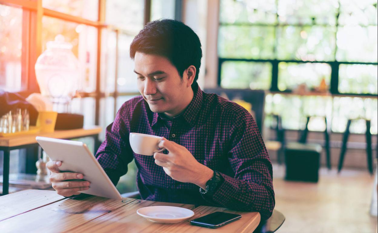 Hombre lee en su tablet y toma café. 