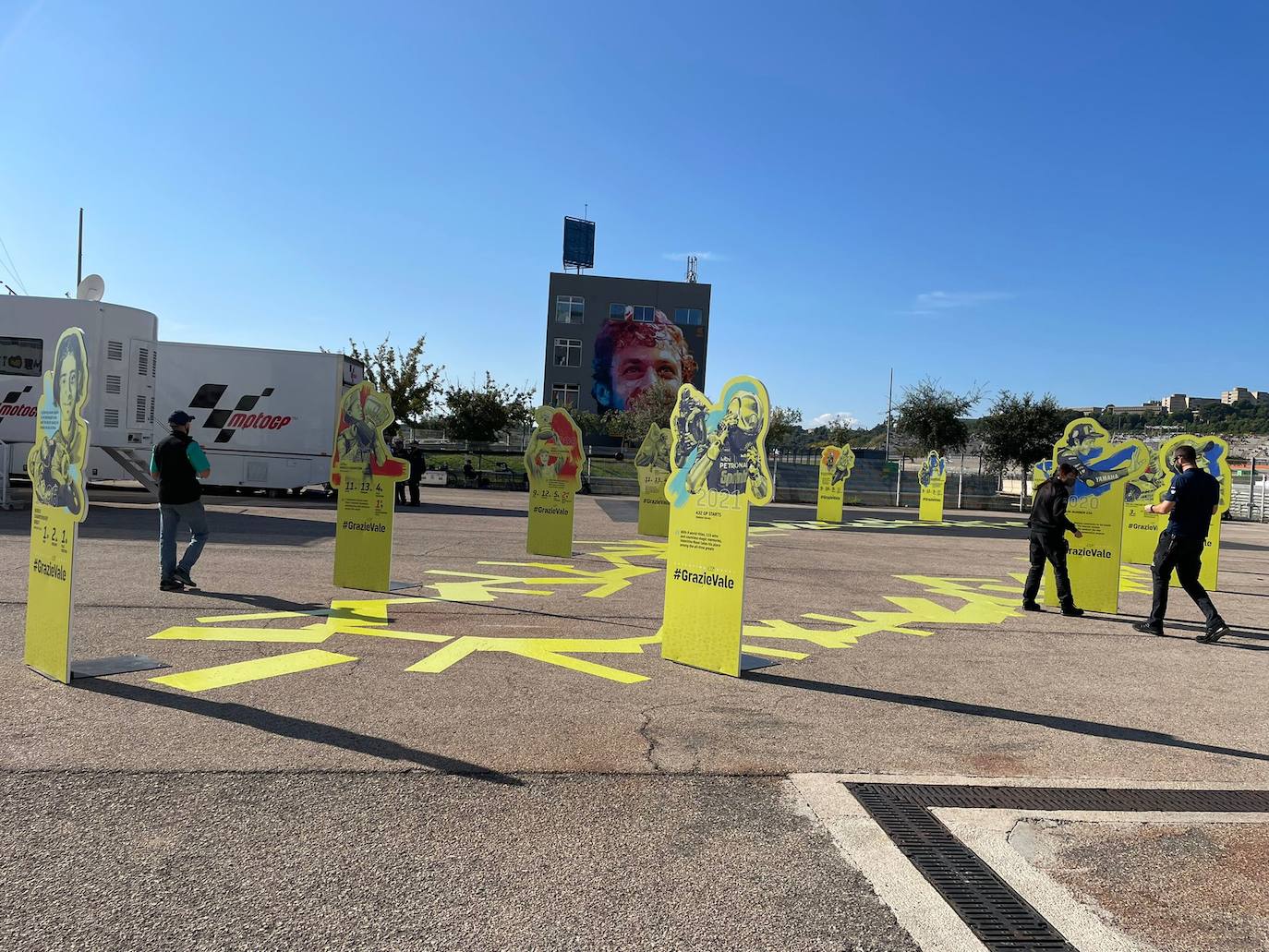 El paddock se ha teñido de amarillo este fin de semana. Como las gradas, que el sábado ya han expresado una muestra de intención de lo que será la carrera de este domingo. No es para nada exagerado afirmar que el 70% de los aficionados lucían merchandising de Valentino Rossi. Entre las muestras de homenaje que se le han dedicado por el momento, destaca la exposición de las nueve motos con las que ha sido campeón del mundo. Al lado está la 'Piazza Valentino Rossi', rotulada con una placa que simula ser de mármol y donde hay unos paneles amarilos que expresan los principales hitos del mito transalpino a lo largo de su carera. Más allá de esto, la mayoría de los camiones de los equipos tienen un panel, del mismo diseño, como muestra de gratitud al piloto por haber potenciado el Mundial de MotoGP durante sus más de 25 años de carrera. El propio piloto, en su mono, luce en la parte posterior este fin de semana un escueto pero representativo: 'Grazie'.