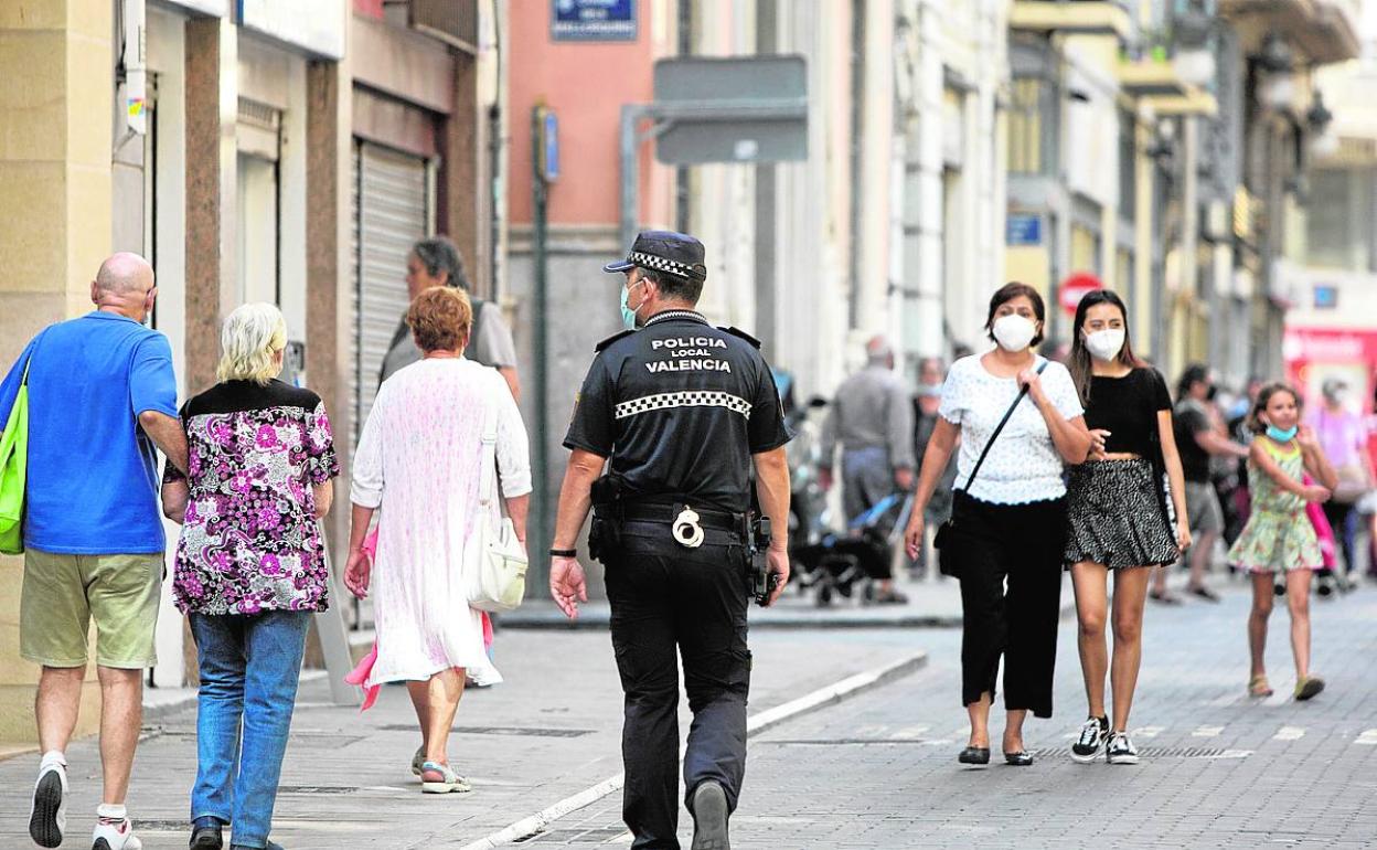 Un policía local camina por una calle de Valencia junto a varios viandantes. 