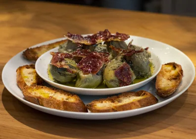 Imagen secundaria 1 - Arriba, estannterías de la Bodega Albarizas. Abajo a la izquierda, su plato de alcachofas con jamón. Abajo a la derecha, una copa de vino blanco seco.