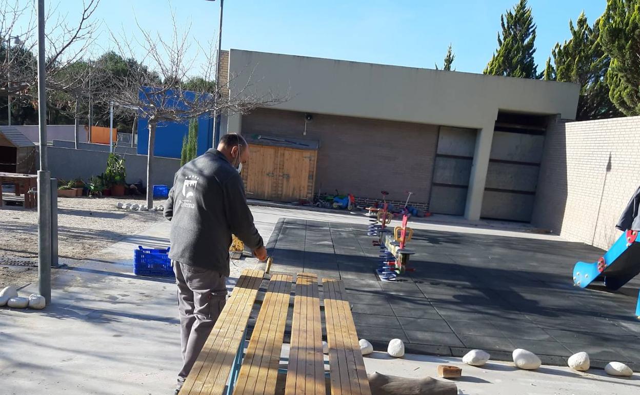 Un operario pinta el banco de un colegio. 