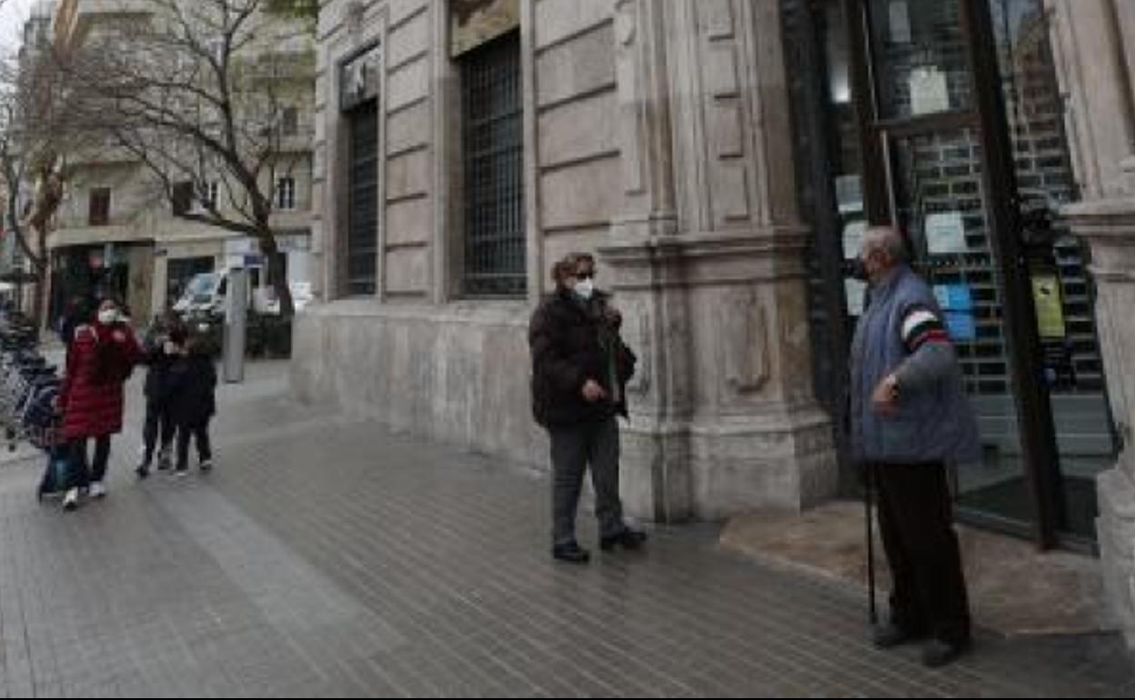 Un grupo de personas mayores esperan en la puerta de una sucursal. 