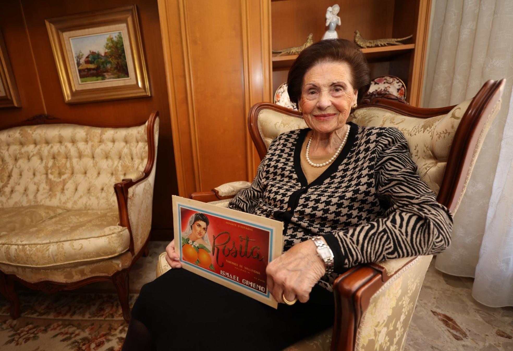 Rosita Gimeno Gimeno, en su casa de Tavernes de la Valldigna, con el original de la etiqueta en la que figura su foto con 20 años. Este formato grande se utilizaba como 'testero', pegado en las cajas de madera. txema rodríguez