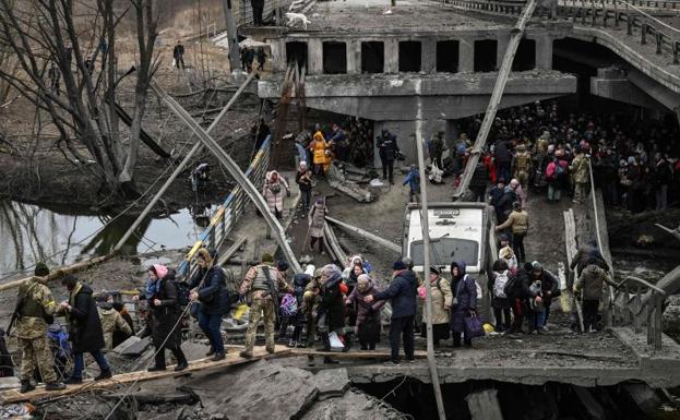 Galería. Soldados ucranianos ayudan a la población a cruzar un puente destruido tras los bombardeos en la ciudad de Irpin.