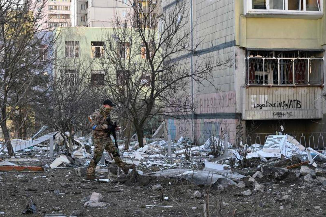 Un miembro de las Fuerzas de Defensa Territorial de Ucrania camina cerca de un bloque de apartamentos dañado.