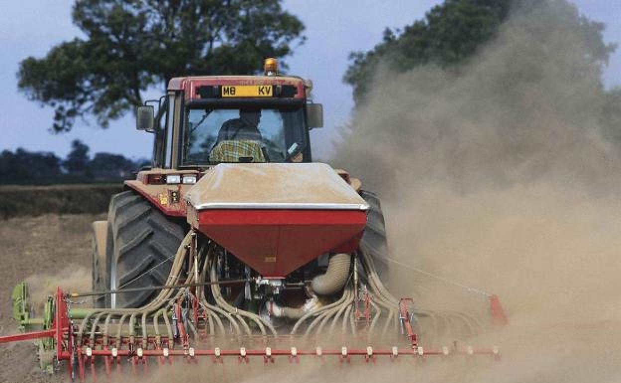 Un agricultor esparce nutrientes químicos en un cultivo con una abonadora enganchada al tractor.