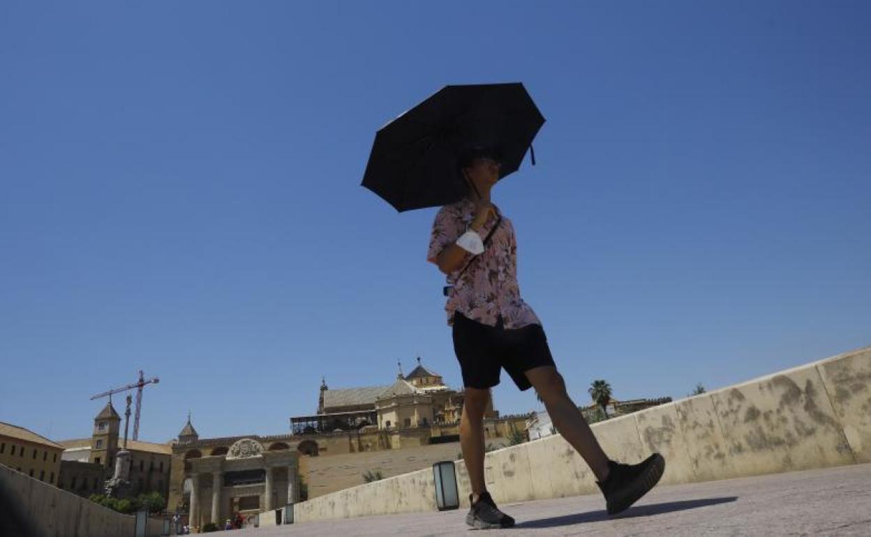 Un turista se protege del sol con un paraguas a su paso por el Puente Romano con la Mezquita-Catedral de Córdoba al fondo