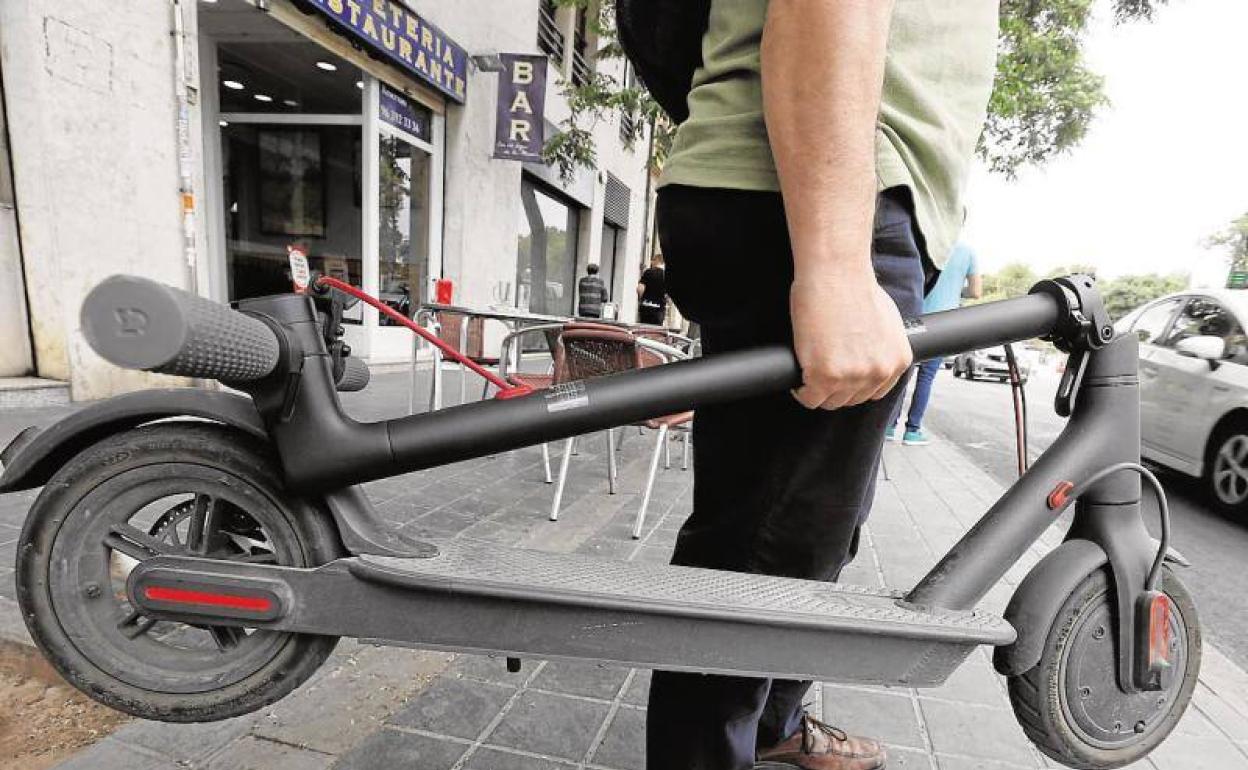 Un hombre lleva en sus manos un patinete eléctrico. 