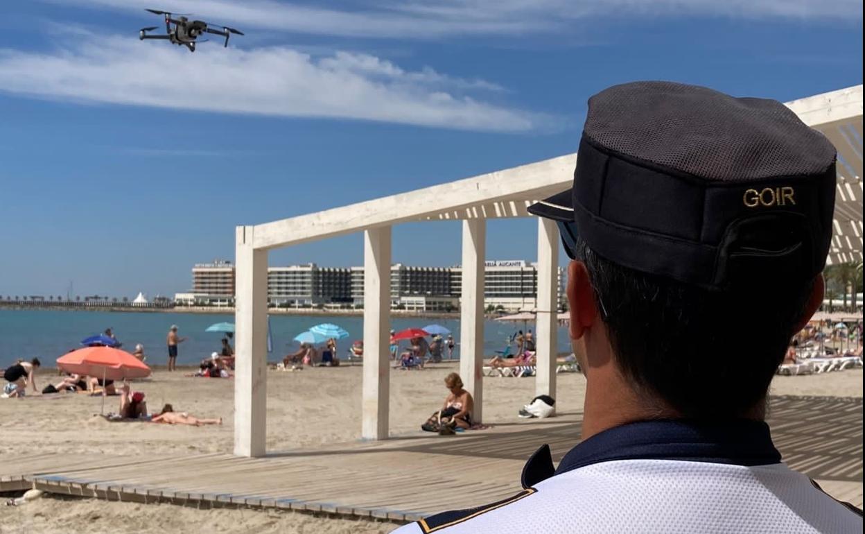 Un agente dirige el vuelo de un dron en la playa del Postiguet de Alicante. 