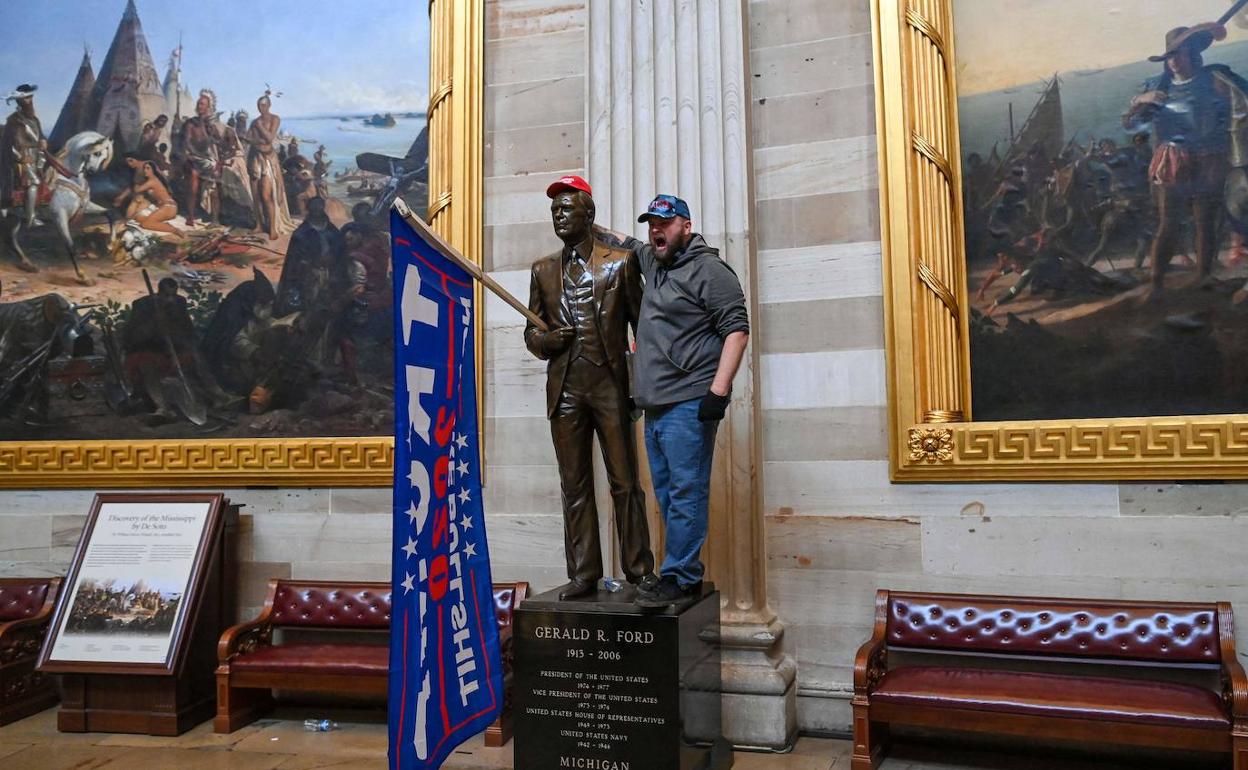 Uno de los asaltantes posando con una escultura del Gerald Ford, al que le han colocado una bandera de la campaña de Trump. 