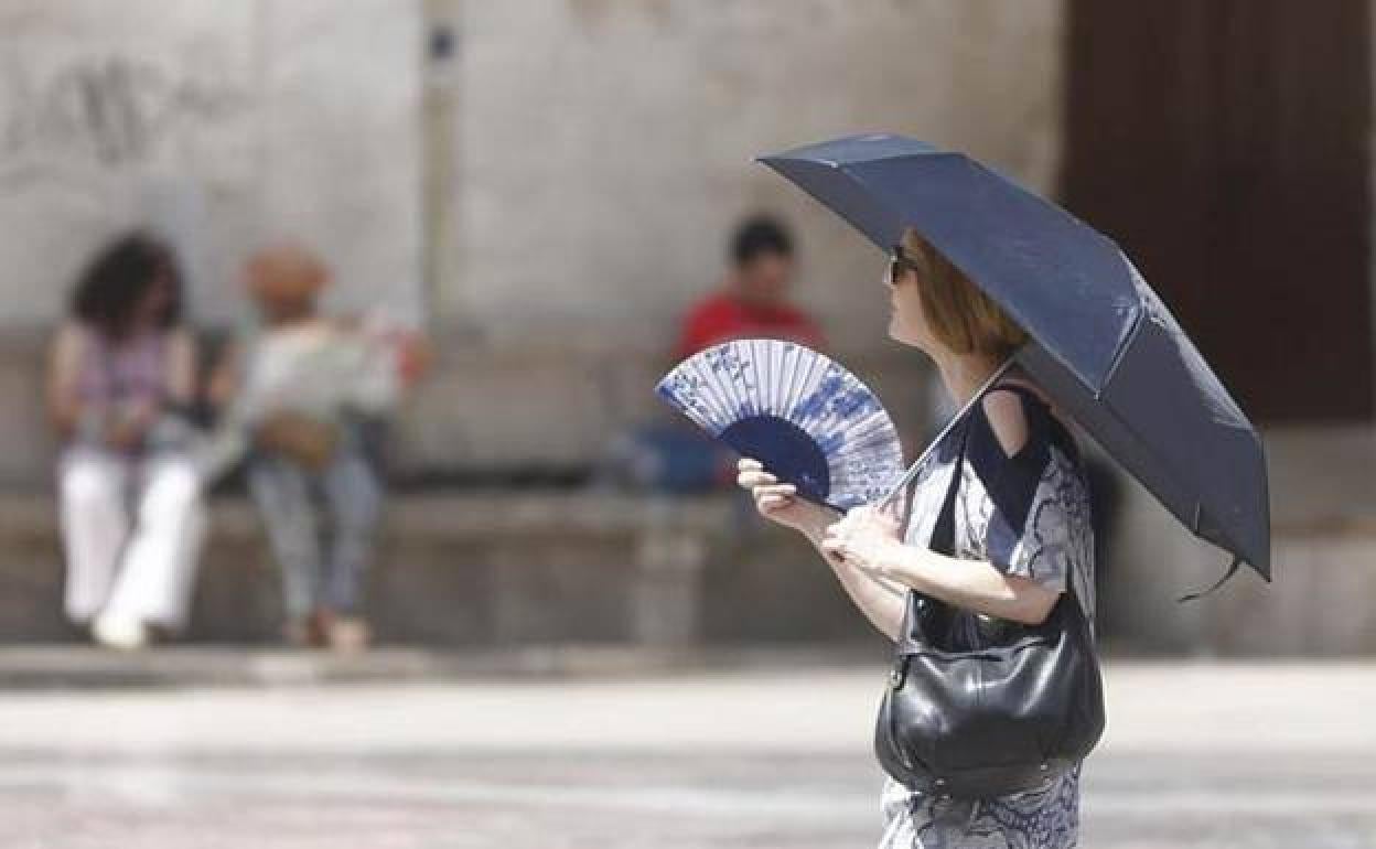 Una mujer pasea por el centro de Valencia con parasol y abanico. 