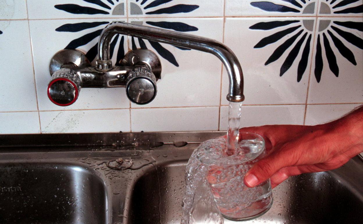 Un hombre llena un vaso con agua del grifo. 