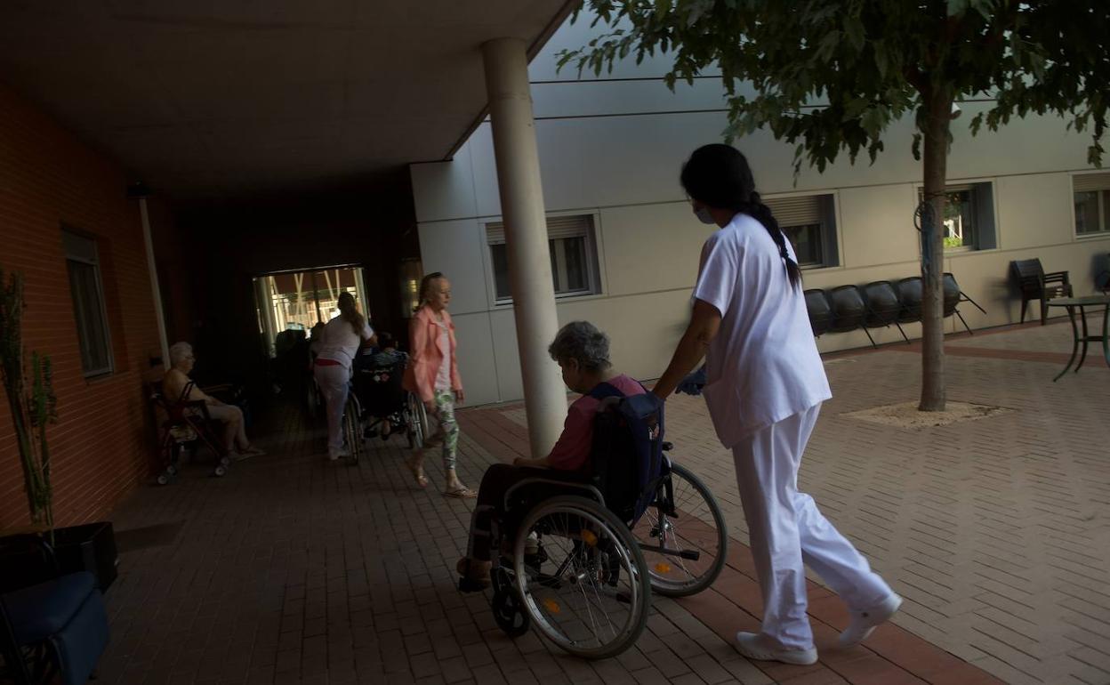 Un trabajador empuja una silla con una anciana. 