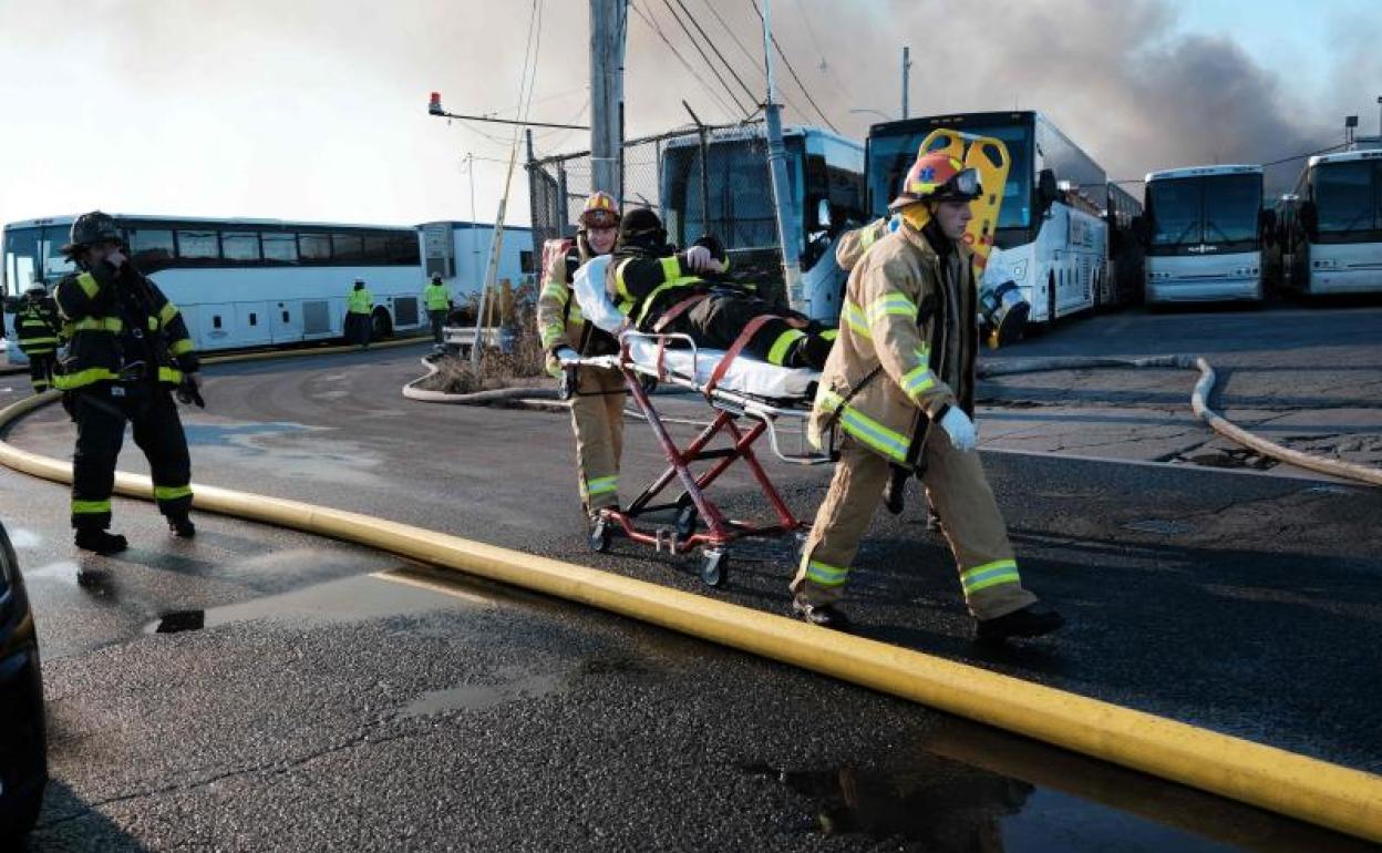 Dos bomberos trasladan en camilla a un compañero herido durante el incendio en el almacén de pruebas de la Policía de Nueva York. 