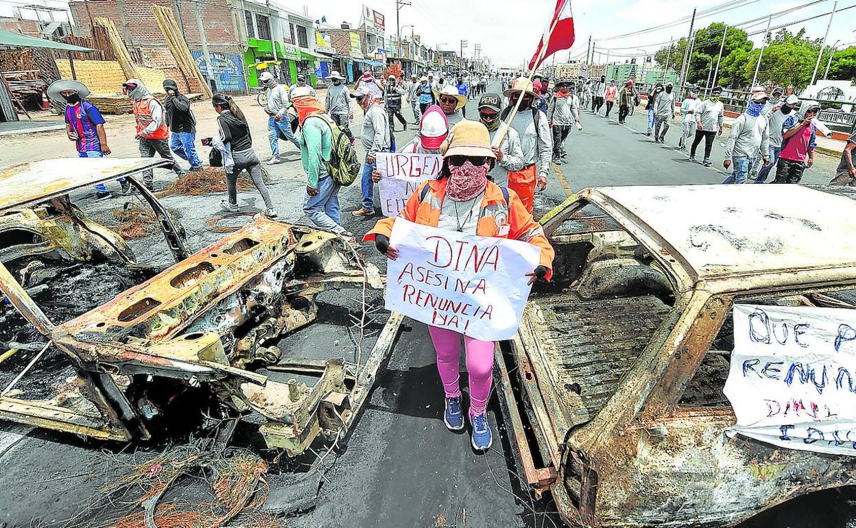 Simpatizantes de Castillo caminan entre dos vehículos incinerados en Arequipa mientras se manifiestan para pedir la salida de Din a Boluarte y el cierre del Congreso.