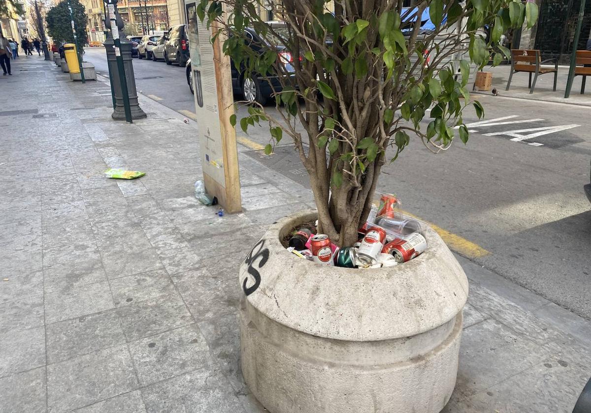 Latas cerveza y basura acumulada en un macetero de la calle San Vicente tras las Fallas.